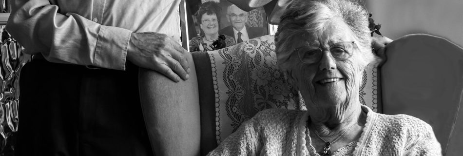 Older couple in their front room with a photo of how they looked years ago